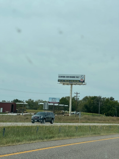 A highway billboard that reads "IS ANYONE EVEN READING THIS?", viewed from the driver's seat on Interstate 70 westbound. It's an ad for a local Dairy Queen.