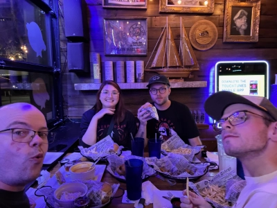 Mike Tarpey eats burgers and appetizers at Captain Mike's restaurant with his partner Beau and the Spragues from Wisconsin. The wall is decorated with naval trinkets like a wood-carved sailboat and a gold framed photo of Captain Mike, presumably.