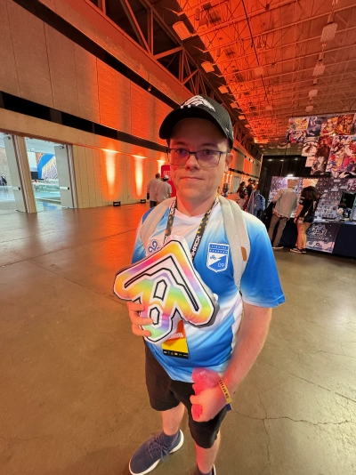 Mike Tarpey holding a rainbow-colored Dance Dance Revolution arrow pillow made by Maiden And The Machine.