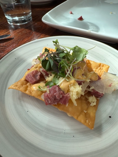 Closeup of a square fried wonton appetizer topped with chopped corned beef, sauerkraut, thousand island dressing, and greens.