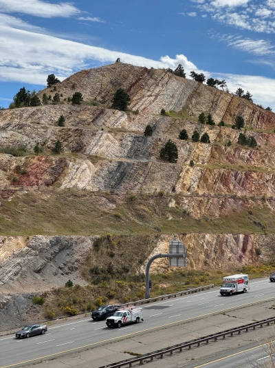 A huge, layered rock formation near Red Rocks Trail in Golden, Colorado. Cars can be seen traveling the highway in the bottom portion of the image.