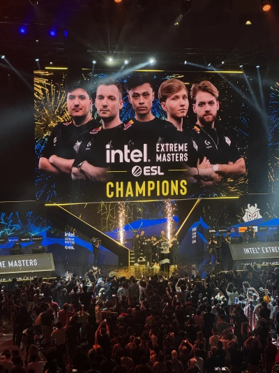 The winning moment from IEM Dallas 2024. Members of G2 Esports stand behind their trophy on-stage after defeating Vitality 2-1 in the best-of-3 series. Their faces are displayed prominently on the big screen above the stage, while smaller yellow pyrotechnics fire off on each side.