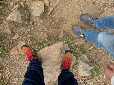 Looking down at our hiking shoes on Lookout Mountain in Colorado. One pair is tan with bright red laces, and the other pair is gray with white accents.