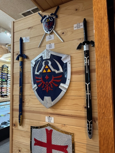 A replica of a Hylian Shield hanging on a natural wood wall in a local sword shop in Estes Park. It's flanked on either side with Master Sword replicas (one blue, one black).