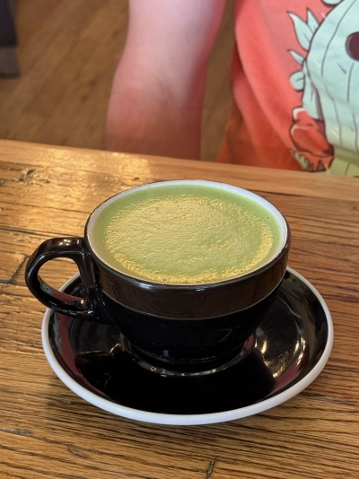 Closeup of a foamy-looking matcha tea, a cool shade of green inside a black cup with a handle.