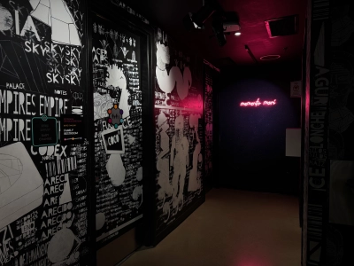 A primarily black-and-white exhibit inside the Meow Wolf in downtown Denver disguises the entrance to the restrooms. The biggest splash of color in the image is a neon sign that reads "memento mori" in a handwritten font.