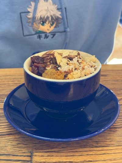 A blue cup of oatmeal topped with dried fruits, nuts, and coconut shavings. The consumer is wearing a light blue Killua hoodie from Hunter X Hunter.