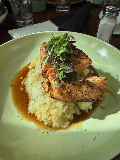 Closeup of a pan seared, bourbon teriyaki salmon cooked to medium temperature, topped with greens and sitting on a mountain of colcannon risotto.