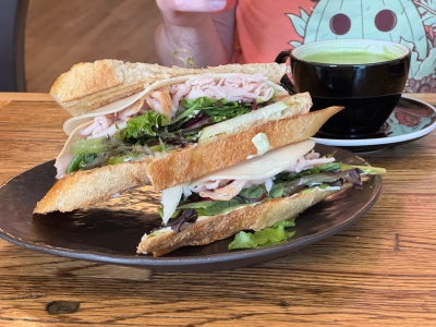 Closeup of a turkey sandwich with cheese, greens, apple slice, and basil mayo. The sandwich is sliced in half, with one half stacked on the toher. There is a long wooden pick holding each half together between two slices of grilled bread.