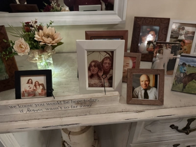 Framed images of family members who are no longer with us, on a white wooden stand with metal drawer handles. The caption in front reads "we know you would be here today, if heaven wasn't so far away".