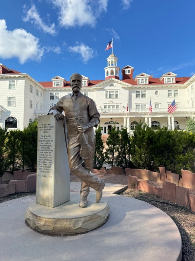 View from the hedge maze in front of the Stanley Hotel. A statue of F.O. Stanley is in the foreground with a quote from 1928. The Stanley Hotel is in the background.