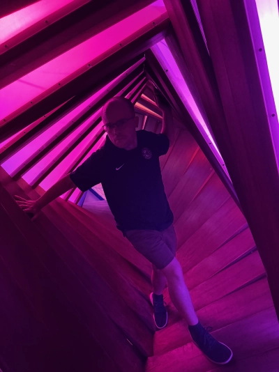 Mike Tarpey traverses a glowing magenta rectangular hallway inside the Meow Wolf in downtown Denver. It twists a full 90 degrees in incremental slices.